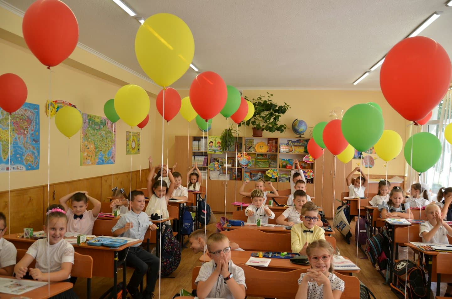 Študenti sedia za stolmi v triede plnej balónov.